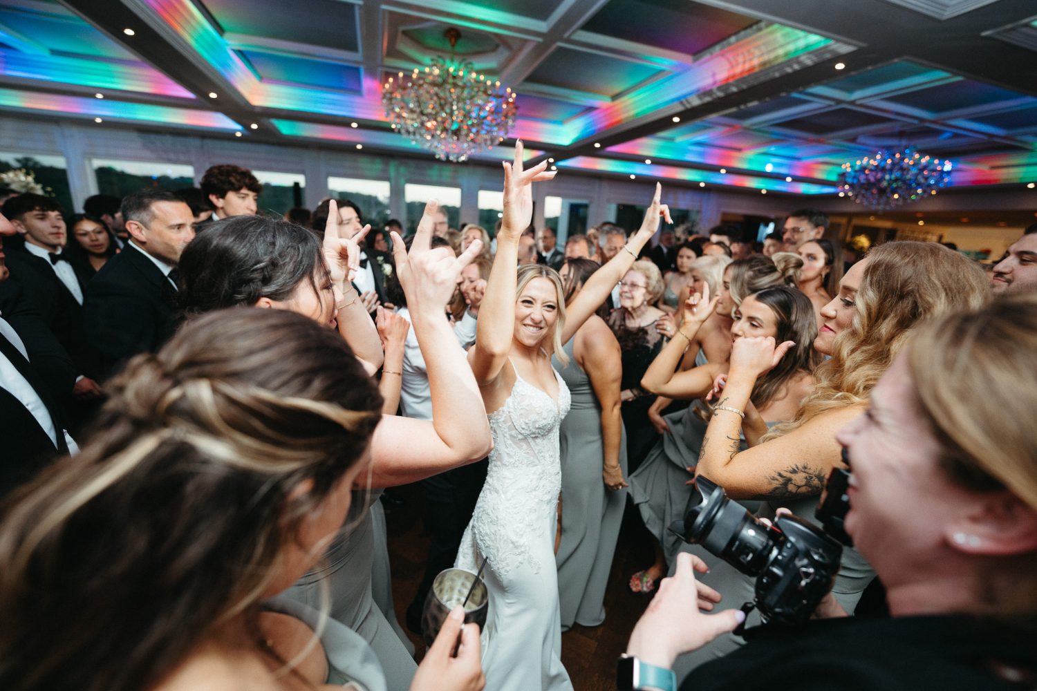 Bride with arms up on a dancefloor under colored ceiling light